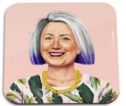 A digital illustration of a smiling woman with short white hair that has blue tips. She wears a white top with green leaf patterns and a large, chunky gold necklace. The background is a soft pink color, reminiscent of the delicate hues often seen in stylish homewares like the Hipstory Coaster Hilary Clinton by Blue Dog Posters.