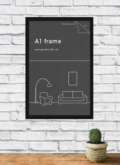 A brick wall features a Blue Dog Posters' Classic Frame A1 Black containing a framed poster with minimalistic illustrations of a floor lamp, armchair, sofa, and picture frame. Below the poster, there's a small round table with a potted cactus on it.