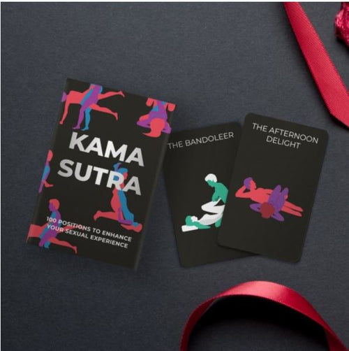 A set of Gift Republic Kama Sutra Cards by Blue Dog Posters, along with two adults-only cards titled "The Bandoleer" and "The Afternoon Delight," are displayed on a dark surface adorned with a red ribbon. The cover features stylized colorful figures in various sexual positions.