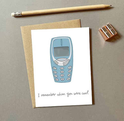 A charming addition to our Giftware Collection, the Nokia Coool Greeting Card by Blue Dog Posters features an illustration of an old-fashioned mobile phone with buttons. Below, handwritten text reads, "I remember when you were cool." The card is blank inside for your personal message and comes with a brown envelope, pencil, and sharpener.