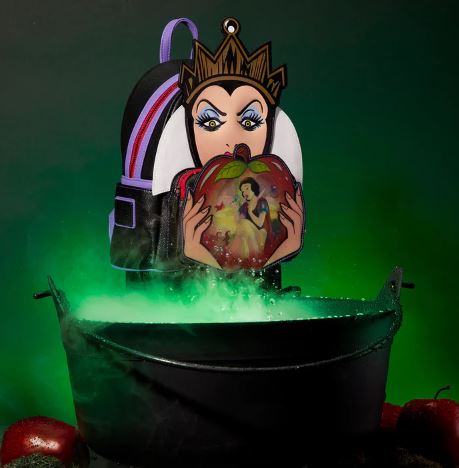 A black cauldron emits green smoke, and behind it is a Snow White Evil Queen Apple Mini Backpack by Blue Dog Posters, featuring the Disney Evil Queen holding a red apple with an image of a princess inside it. Red apples surrounding the cauldron add to the eerie atmosphere.