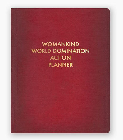 A red notebook from Blue Dog Posters called the Womankind World Domination Planner, featuring a cover stamped in gold foil with the phrase "WOMANKIND WORLD DOMINATION ACTION PLANNER" in uppercase letters. This practical journal includes both dotted and ruled pages.